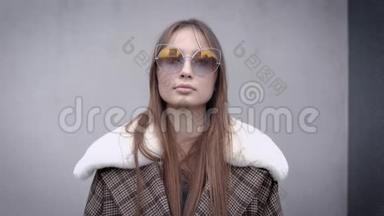 秋天，漂亮的黑发模特站在户外，她穿着一件时髦的保暖外套，带着毛皮领子和太阳镜